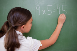 This is a picture of a girl writing multiplication of 9 times 5 on a chalkboard.