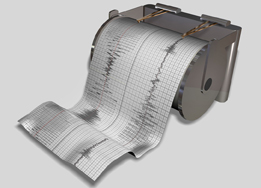 This is an image of a seismograph machine. There is a needle that moves back and forth on grid paper to indicate the amplitude of seismic waves.