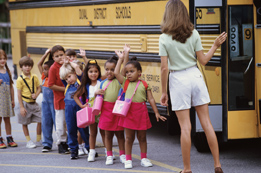 This is a photo of young children lining up for a school bus. 