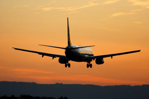 A photograph shows the back end of a jet airplane as it lands on a runway during sunset.