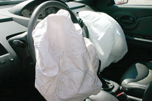 A photograph shows the inside of a vehicle where airbags in the steering wheel and in the dash on the passenger side have both deployed.
