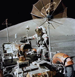 An astronaut standing next to a wheeled vehicle with assorted equipment is shown in this image.
