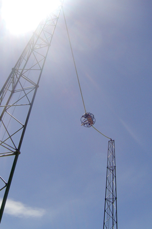 A photo shows a cage in the middle of two support posts and suspended in mid-air by two long bungee cables. 