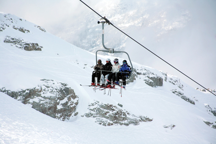 A photograph shows four skiers riding a quad chairlift at a downhill ski resort.