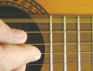 A close-up photograph shows fingers plucking the strings on an acoustic guitar.