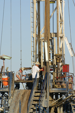 Two men wearing hard hats are seen working on a oil drilling platform in this photograph.