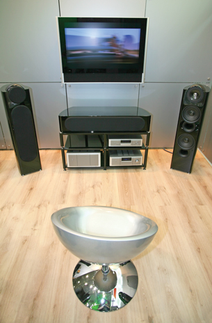 A photograph shows a chair set in front of an entertainment centre. The entertainment centre includes a television set. On either side of the TV are two speakers.