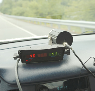 The inside of a police cruiser is shown in this photograph. A radar gun is aimed at a motorist on a highway.